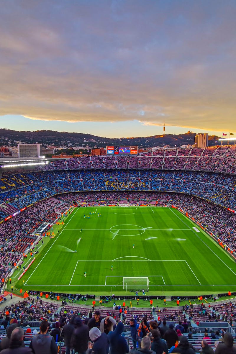 Aerial view of Camp Nou stadium filled with spectators during a football match at sunset in Barcelona, Spain.